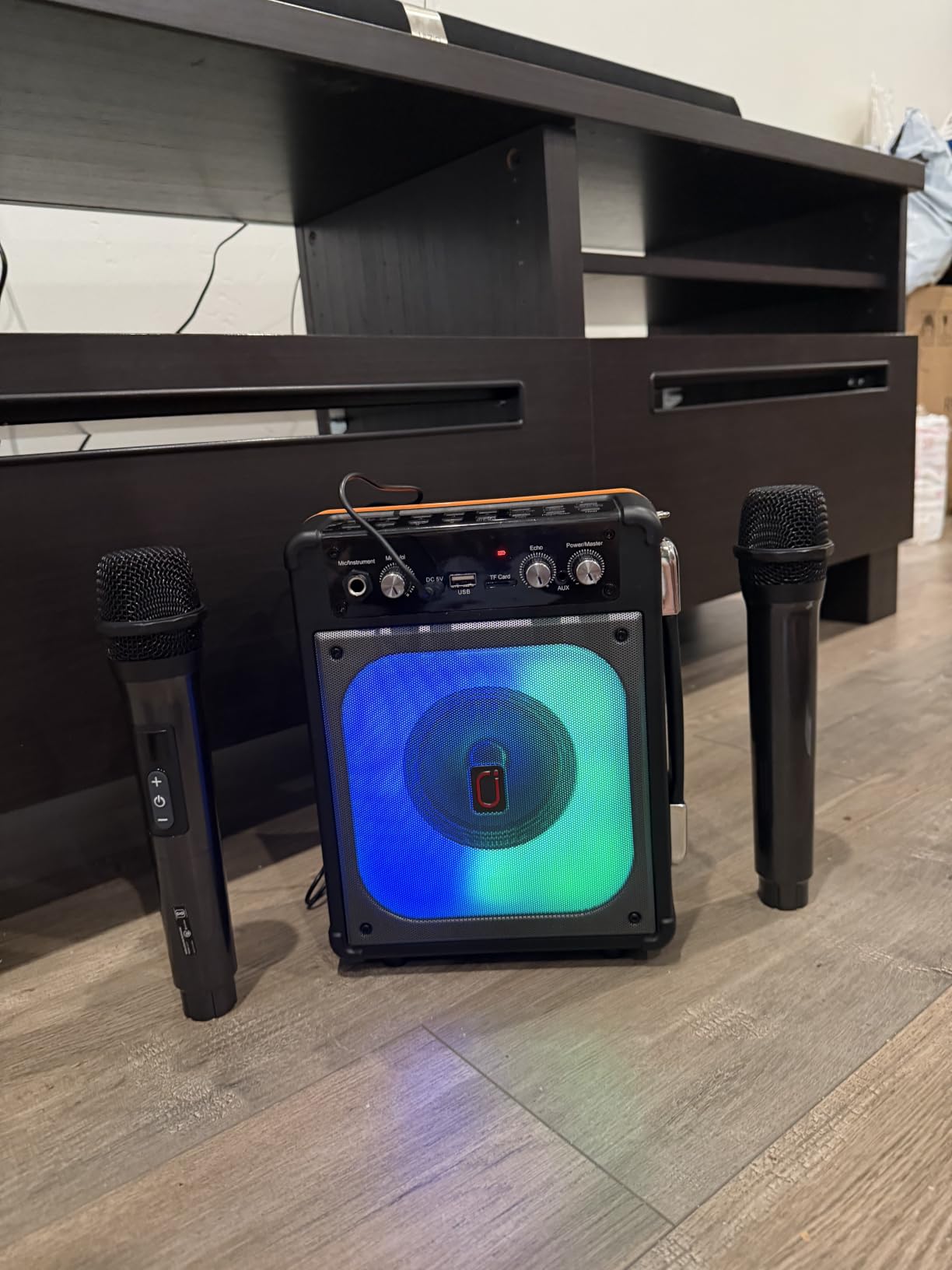 HWWR karaoke machine lit blue and green under a TV stand with a microphone standing on each side