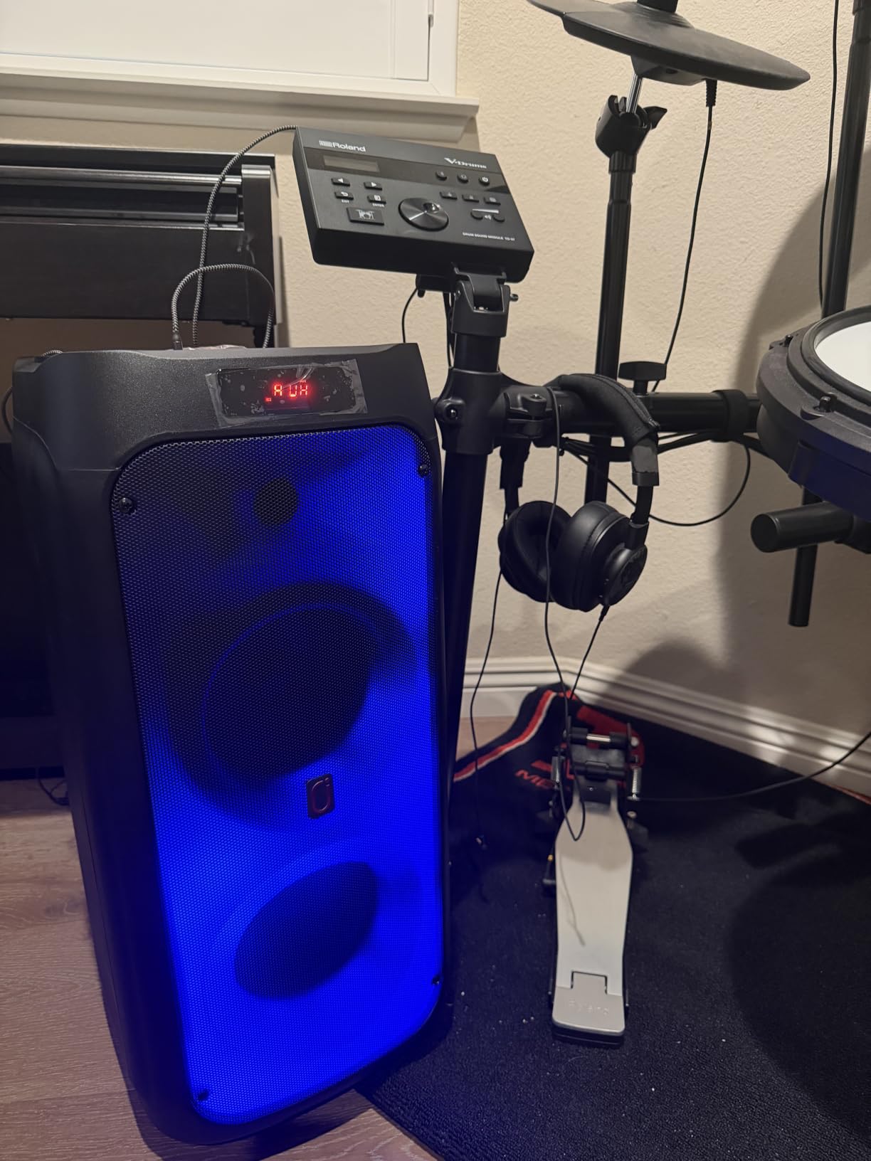 Tall dual-woofer HWWR karaoke machine glowing blue beside an electronic drum kit
