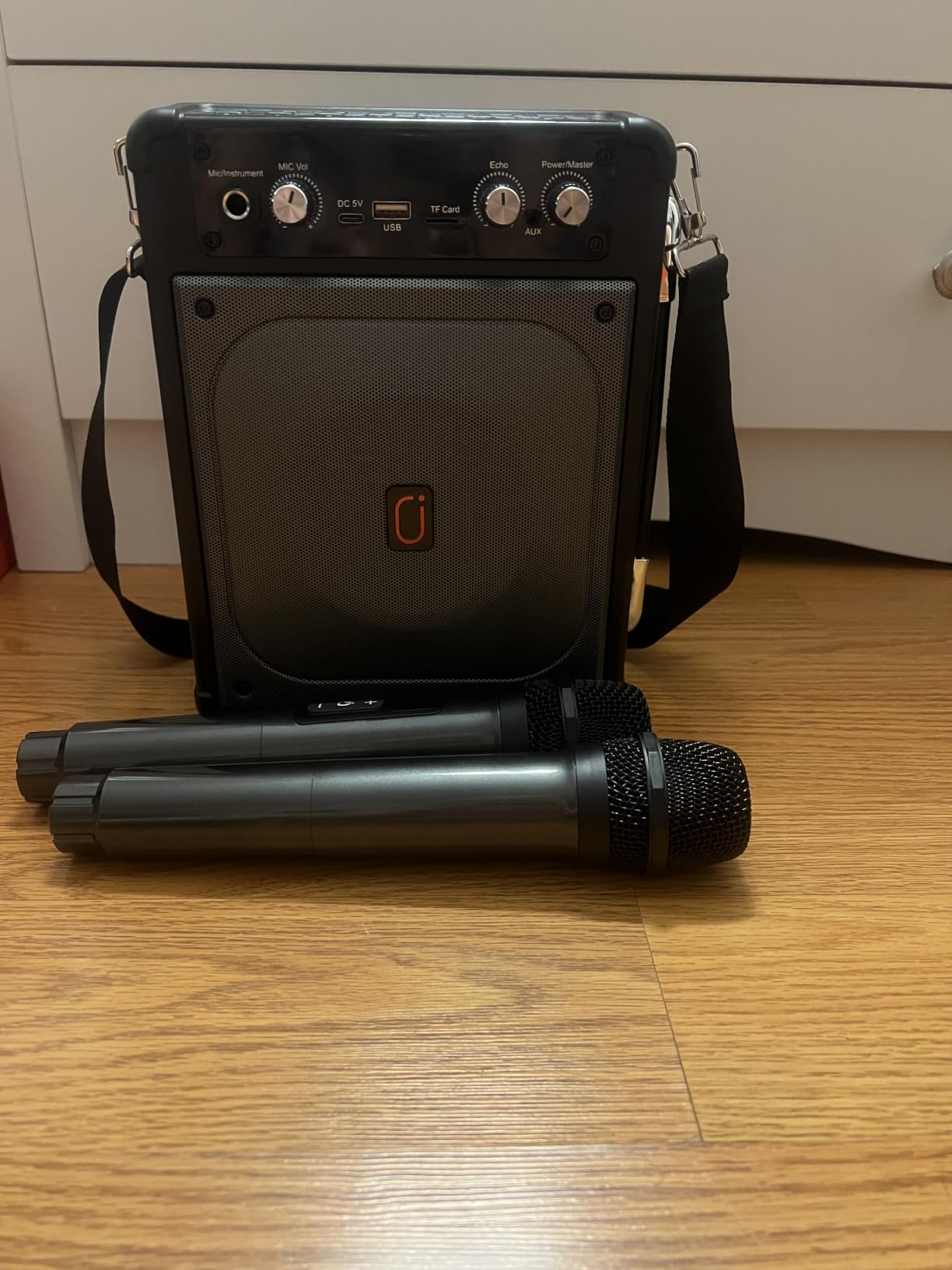 HWWR karaoke machine with its shoulder strap and two wireless microphones on a wood floor